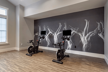 Two exercise bikes are placed in front of a wall mural at Reserve by the Lake, TX, 77084